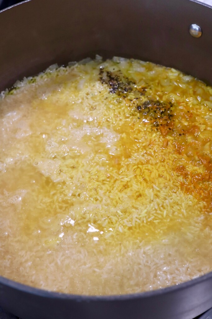 white rice in skillet with seasonings and broth