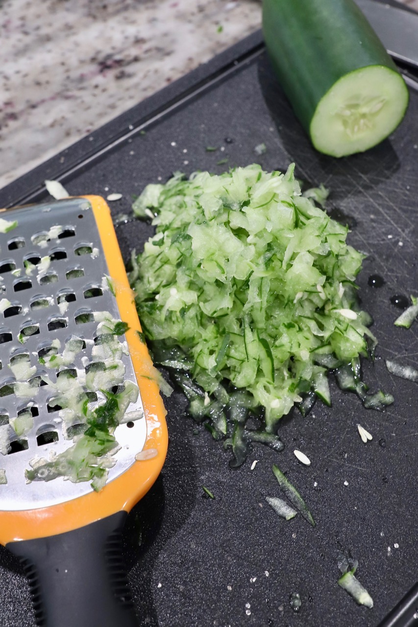 grated cucumber on cutting board with hand grater