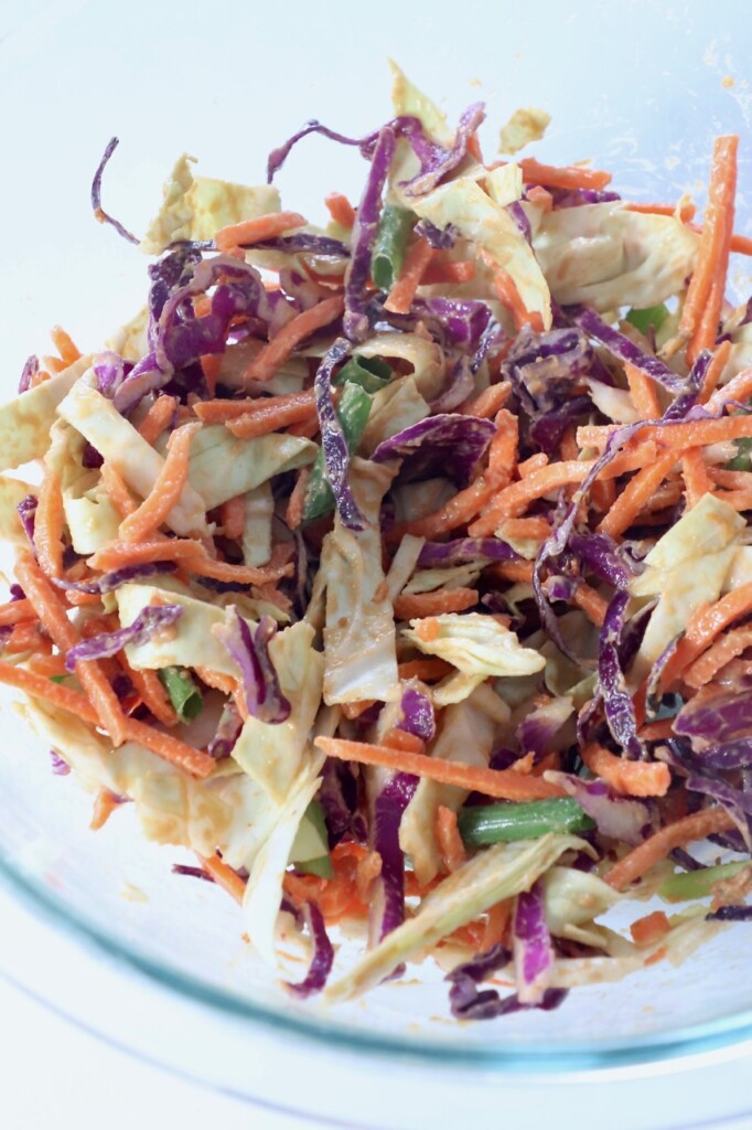 slaw tossed with peanut sauce in glass bowl