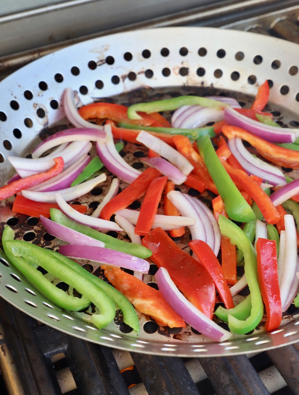 sliced bell peppers and onions in grill basket on grill